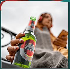Social media photo: a person holding an Amstel bottle, sitting in a car